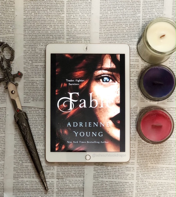 Picture of an iPad with Fable book cover, showing a woman with red hair and blue eyes. Next to the iPad on the left are jeweled scissors and on the right 3 candles