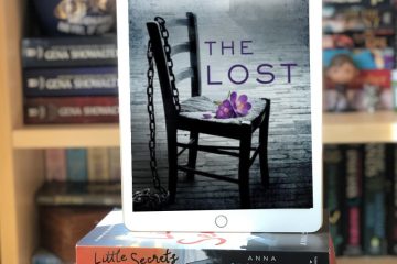 Ipad resting on stack of books. The iPad shows the cover of The Lost by Natasha Preston. The cover image is a grey chair with purple flowers sitting on the seat, a chain hangs over the back of the chair.