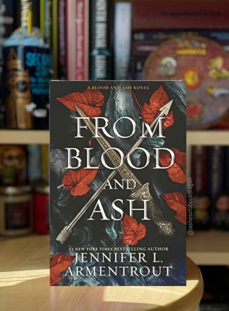 Imagie showing a book on a wooden stool in front of a bookcase. The book cover reflects a sword and arrow crossed together with red leaves behind it