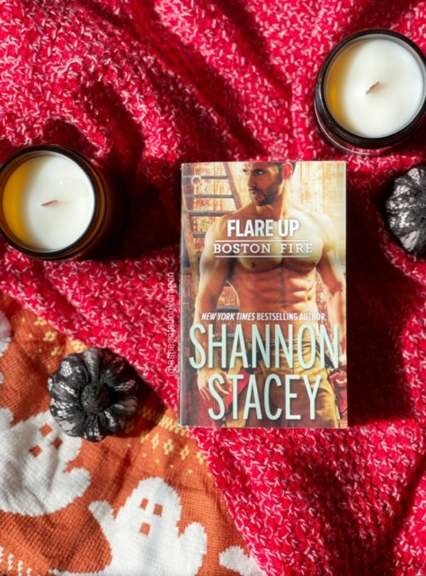 Photo of a Shirtless an on a book cover laying on a red blanket with two candles and two small pumpkins on either side
